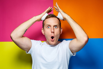 portrait of a young cheerful guy on a multi-colored background, dressed in a white T-shirt, poured hair foam in his hands, creates a fashionable hairstyle