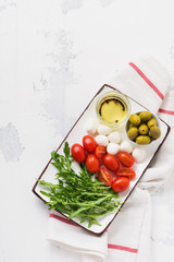 Mozzarella, cherry tomatoes and arugula served in white ceramic rectangular plates with olive oil over grey texture background. Flat lay
