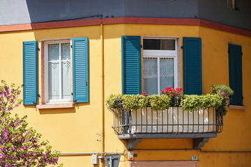 Fototapeta na wymiar Italian windows on the yellow wall facade with open green color classic shutters with blooming flowers and balcony