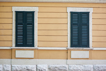 Two Italian windows on the yellow wall facade with closed green color classic shutters