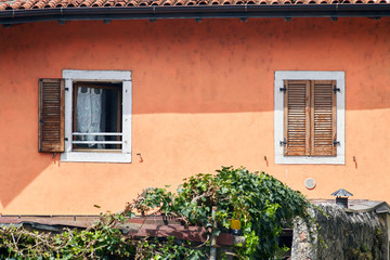 Fototapeta na wymiar Two Italian windows on the red wall facade with open and closed brown color classic shutters