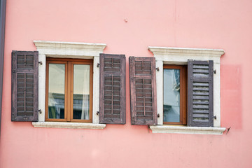 Two Italian windows on the rose wall facade with open and closed brown color flaky classic shutters