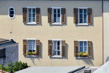 Italian windows on the sandy-yellow wall facade with open brown color flaky classic shutters