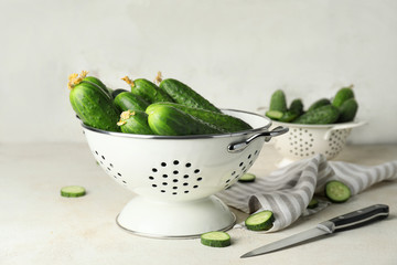 Colander with green cucumbers on table