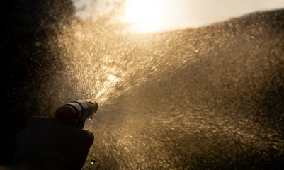 Hand holding garden water hose spray gun with water splash against sun. Beautiful effect of water splashes