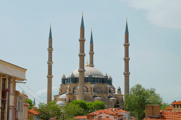 Fototapeta na wymiar Sunny, clear blue sky. Minarets of light yellow limestone, marble, dark blue, gray domes on roof of mosque. Bright juicy fresh green leaves on trees. Copy space. Selective focus Turkey, Edirne