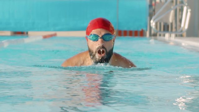 Front side shot of professional swimmer performing breaststroke during training in swimming pool.