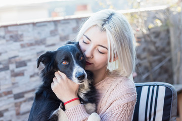 Beautiful caucasian woman hugging her dog pet sitting on chair at home terrace