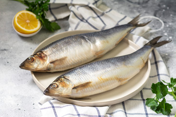 Herring on a white plate on a light gray table. Salted fish