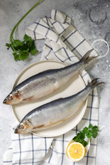 Herring on a white plate on a light gray table. Salted fish