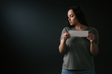 Naklejka premium Front view of sad plus size girl holding empty card on black background