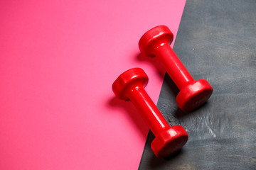 Conceptual fitness and healthy sport background with pink dumbbell on pink background. Flat lay top view with copy space.