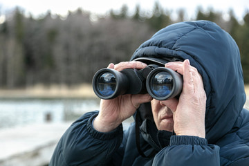 Fototapeta na wymiar A man on the riverbank is looking through binoculars