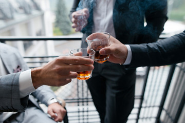 Close up of three hands of men in suits clink glasses of whiskey drink together in restaurant. Wedding day. Business concept. Alcoholic beverage