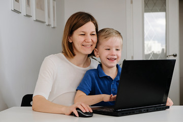 A young woman and her little son sit a home during quarantine and study in the internet school using a computer. Social distance