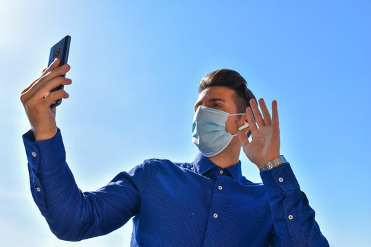 Quarantined Man Wearing Surgical Mask, With Blue Shirt Making A Video Call Through The Mobile, Covid-19