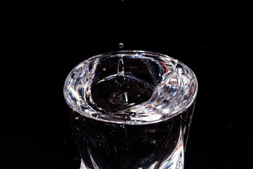 Black background is a glass in which a drop of water falls. Splashing water on glass