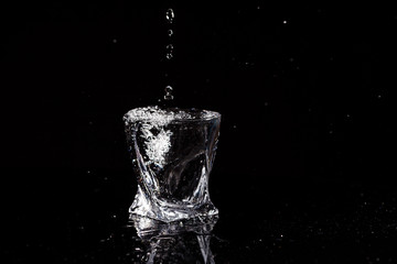 Black background is a glass in which a drop of water falls. Splashing water on glass