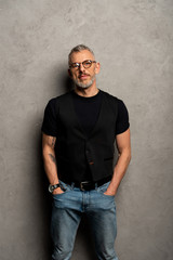 Obraz premium tattooed businessman standing with hands in pockets on grey