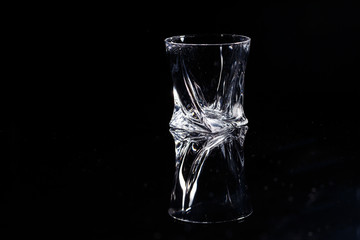 Black background stands a clean glass with reflection on a glass table. Facets on a Glass Cup