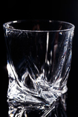 Black background stands a clean glass with reflection on a glass table. Facets on a Glass Cup