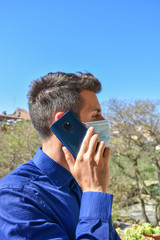 Businessman wearing a blue shirt and a surgical mask, calling and giving instructions with the mobile phone from home for the coronavirus