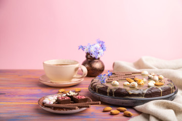 Homemade chocolate brownie cake with caramel cream and almonds with cup of coffee on a colored and pink background. Side view, selective focus, copy space.