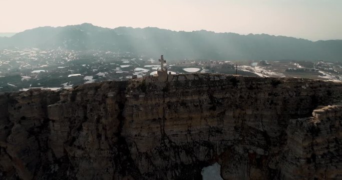 Aerial pull back drone view of cross on mountaintop to reveal Akoura church building, Lebanon