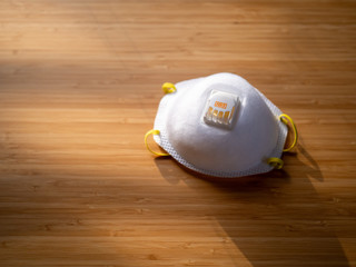 Sun hitting a white N95 face mask with a breathing valve on a wood table. 