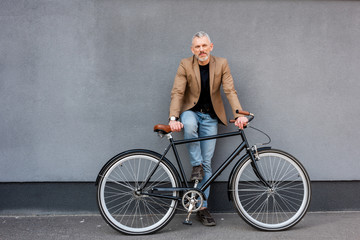 Fototapeta na wymiar handsome businessman in blazer and jeans standing near bicycle outside