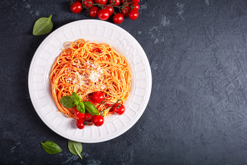 Spaghetti with tomato sauce and cherry tomatoes with basil on a dark background
