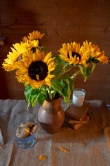 A bouquet of bright sunflowers in a clay jug, books, a glass of milk and a bowl of cookies.