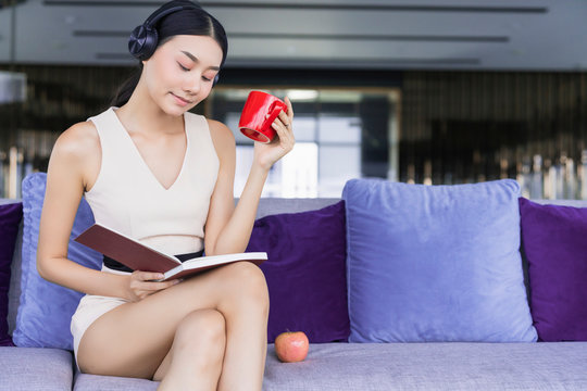 beautiful asian female woman relax enjoy reading book with hot drink coffee and notebook laptop working at home quarantine moment social distancing ideas concept