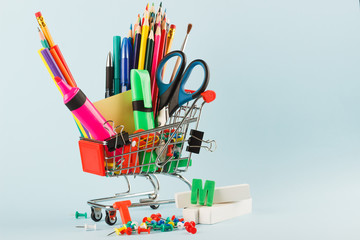 Shopping cart with different stationery on the blue background