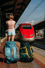 A girl with two Hiking backpacks and a red high-speed train arriving at a station in Italy | PADUA, ITALY - 29 JULY 2019.