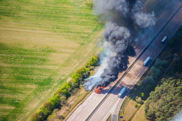 Fototapeta na wymiar Fire on highway - strong black smoke rises to the sky, flames are visible - two trucks caught fire on a highway and burn out completely - aerial view 