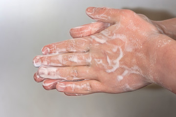 Hands of a young guy in soap foam on a grey background. Hand washing. Minimal hygiene, virus protection concept.