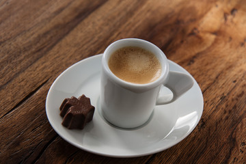 A cup of espresso with a chocolate candy maple leaf shaped on wooden background