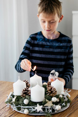 Young boy lighting the first candle on Advent Wreath on the first Sunday in December. Celebrating...