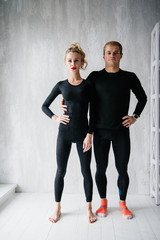 The guy and the girl in tracksuit. Black sports uniform. Male and female athletes. Pumped up body. Triathlon. Morning work-out. Set of exercises for body. Classes in pair. Workout together at home.