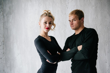 The guy and the girl in tracksuit. Black sports uniform. Male and female athletes. Pumped up body. Triathlon. Morning work-out. Set of exercises for body. Classes in pair. Workout together at home.