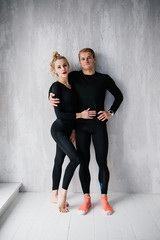 The guy and the girl in tracksuit. Black sports uniform. Male and female athletes. Pumped up body. Triathlon. Morning work-out. Set of exercises for body. Classes in pair. Workout together at home.