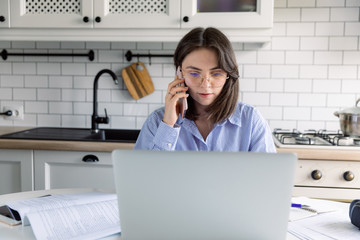 Young beautiful woman works from a home with a laptop on a white desk as a freelancer. Working home concept - girl with smart phone, laptop and business reports.