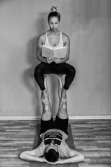 Couple practicing acro yoga in studio, woman reading a book. Acro yoga concept. Pair yoga. Yoga flexibility class workout.