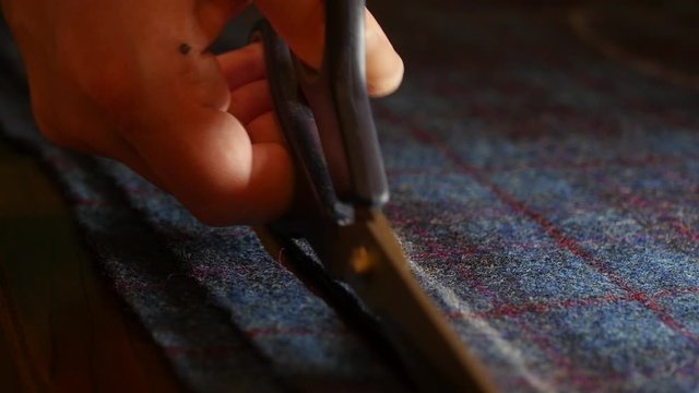 Cutting tweed whilst sewing : Tailor cutting fabric with shears at table in atelier, closeup of tailoring process. Closeup of designer working cutting fabric for a new coat with textile