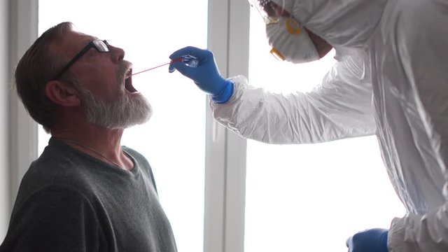 Rapid Test Covid 19, Sampling From A Representative Of A Risk Group. An Elderly Man Takes A Coronovirus Test. A Doctor In A Protective Suit Takes A Swab From The Throat. Non-invasive Testing Method