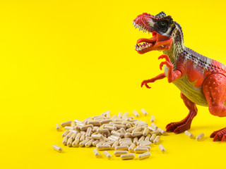 Maca powder in capsules on yellow background with funny toy dinosaur above the pills. Food...