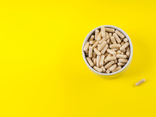 Maca powder in capsules in beige bowl on monochrome yellow background. Food supplement from Peru - 342369667