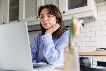 Young beautiful woman works from a home with a laptop on a white desk as a freelancer. Working home concept - girl with smart phone, laptop and business reports.