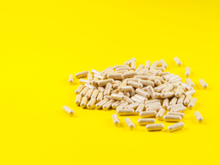 Maca powder in capsules on monochrome yellow background. Food supplement for energy boosting.
